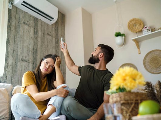 Couple at home looking frustrated with a wall-mounted heat pump that isn't working