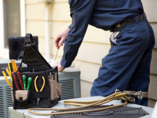 HVAC technician with a tool bag working on outdoor AC units beside a house