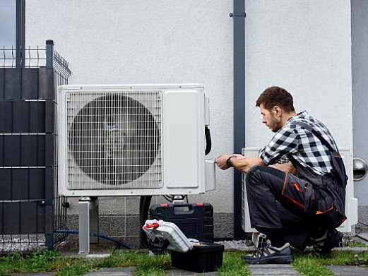 Technician working on a heat pump's outdoor unit next to a house
